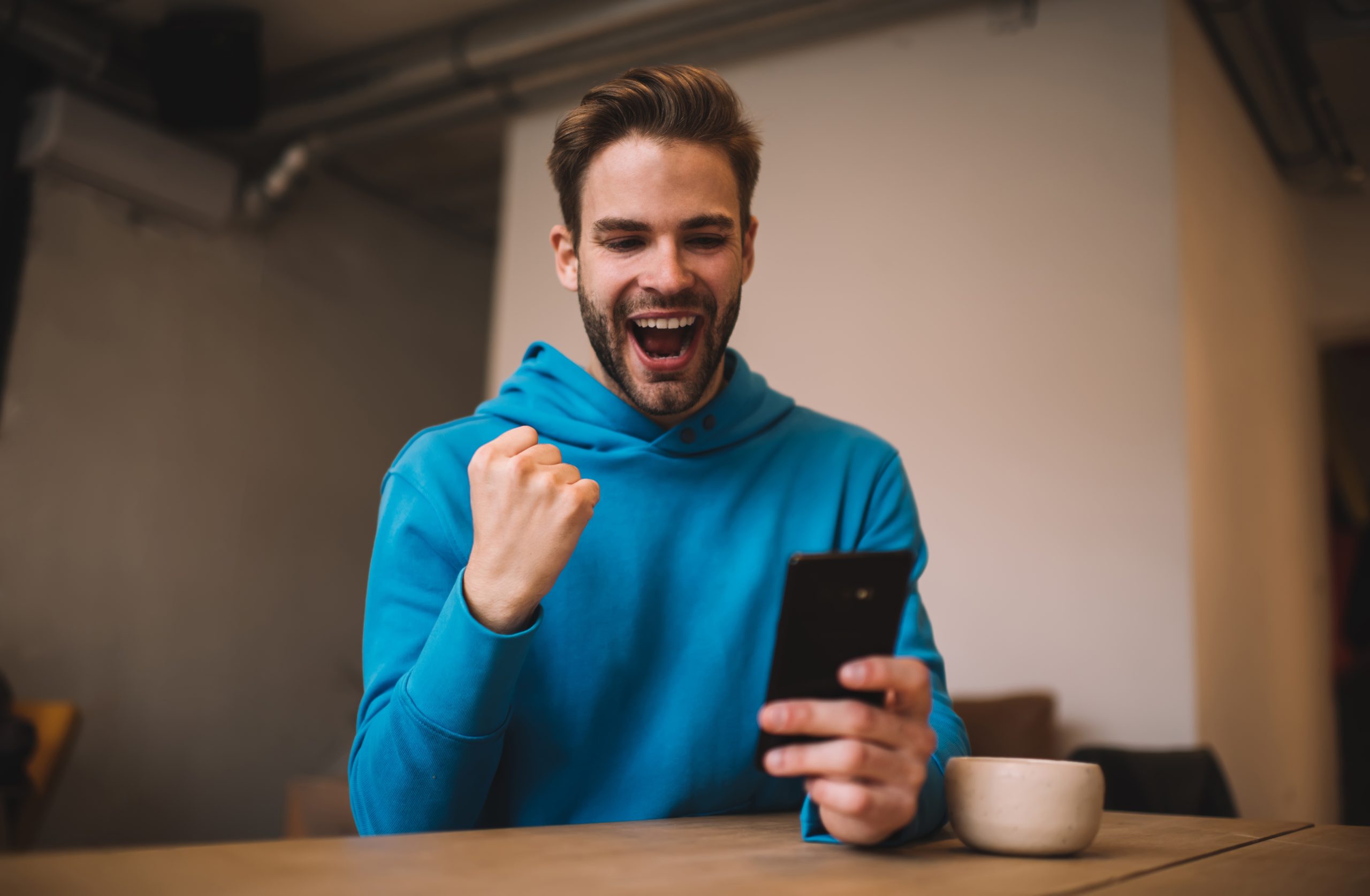 Overjoyed hipster guy rejoicing while reading received email news happy with win in sports betting, cheerful Caucasian blogger celebrating own popularity of influence vlog in social networks